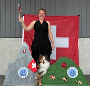 Sheltie staat met eigenaar voor de Zwitserse vlag tijdens de Open European Championships dogdance